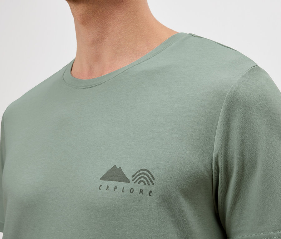 Zbliżenie mężczyzny w jasnozielonej koszulce z małym logo "Explore".