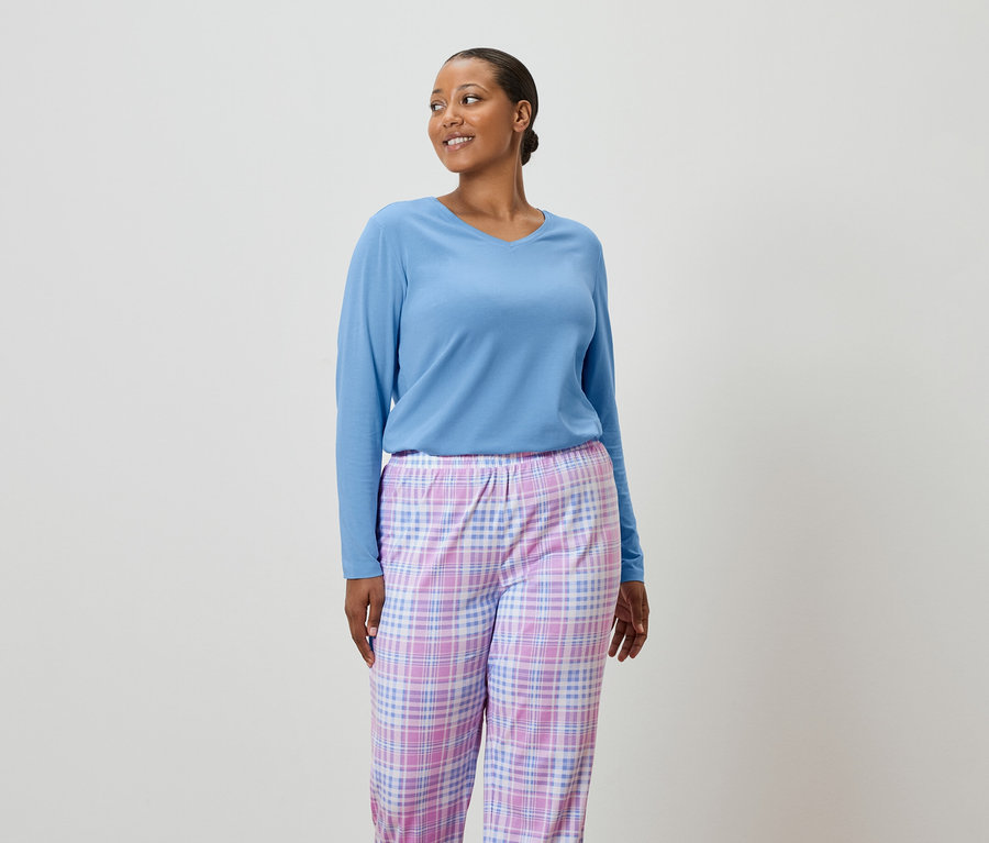 Kobieta ma na sobie jasnoniebieski sweter i spodnie od piżamy w kratę.