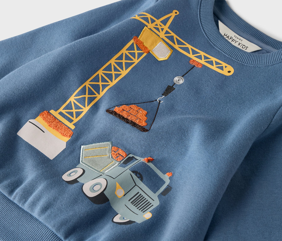 Na niebieskiej bluzie znajduje się żółty żuraw stojący nad ciężarówką z kołami.