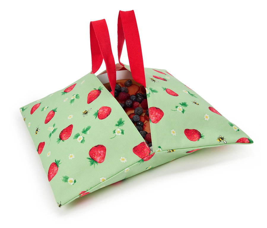 Ciasto truskawkowe w zielonej torbie materiałowej we wzór truskawek z czerwonymi uchwytami.