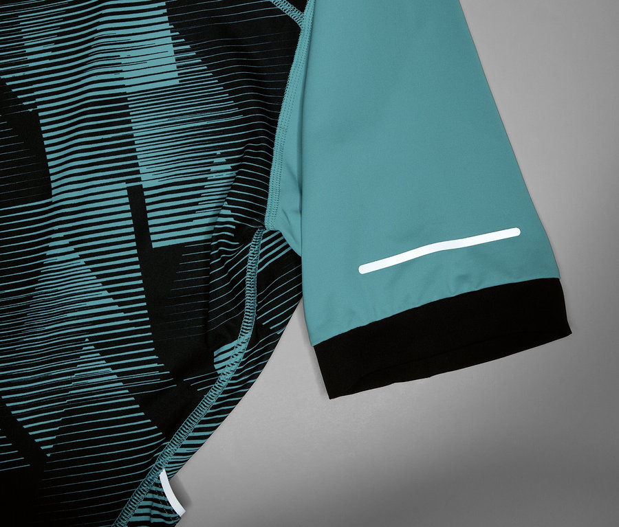 Zbliżenie na koszulkę rowerową z turkusowym rękawem, czarnym mankietem i odblaskowym paskiem.