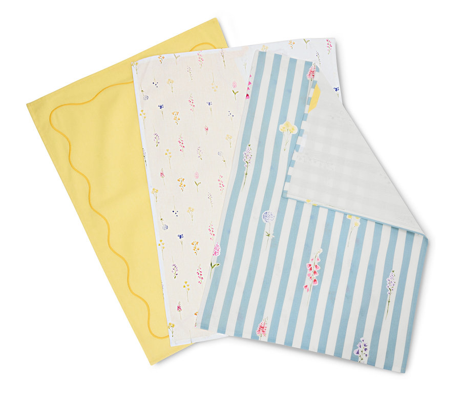 Trzy ściereczki leżą na sobie: żółta z falistym brzegiem, kremowa we wzory kwiatowe oraz niebiesko-biała w paski z kwiatami.