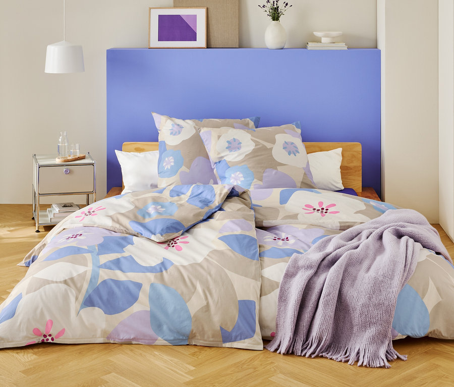 Sypialnia z łóżkiem przykrytym pościelą w kwiaty i fioletowym kocem.