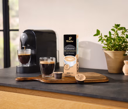 Ekspres do kawy nalewa kawę do szklanki obok opakowania kapsułek Cafissimo Decaffeinato.