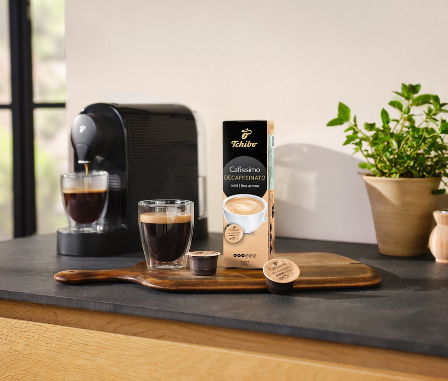 Ekspres do kawy nalewa kawę do szklanki obok opakowania kapsułek Cafissimo Decaffeinato.
