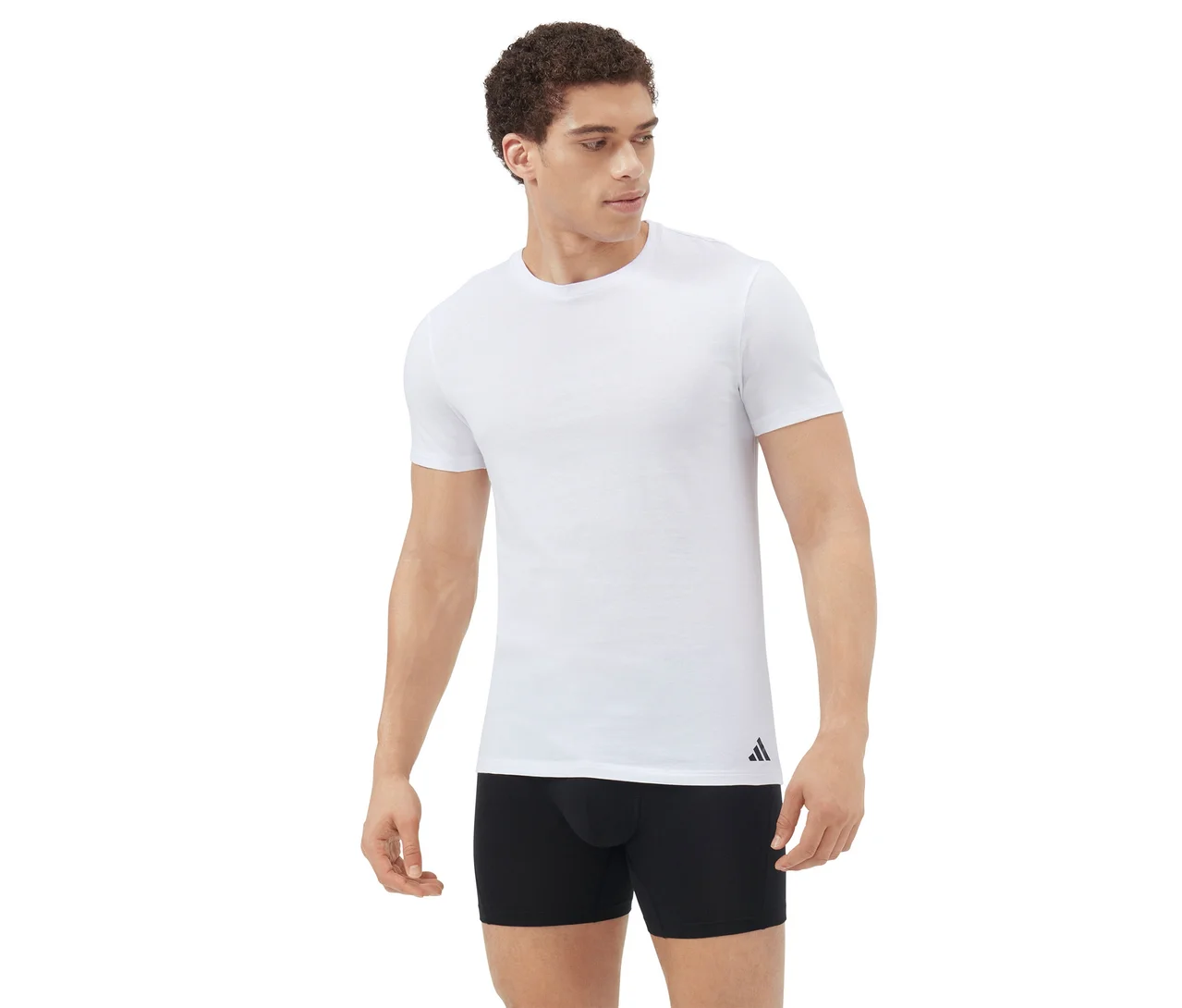 Mężczyzna stoi, ubrany w biały T-shirt z krótkim rękawem i czarne bokserki, patrzy w prawo na białym tle.