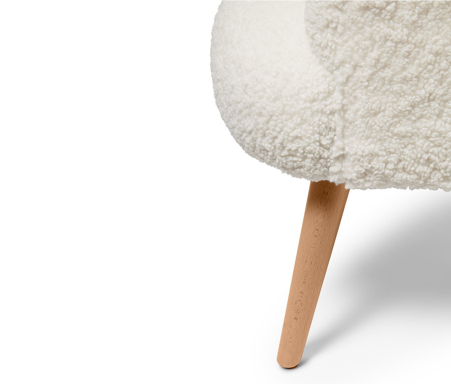 Detal fotela z tkaniny bouclé z drewnianą nogą.