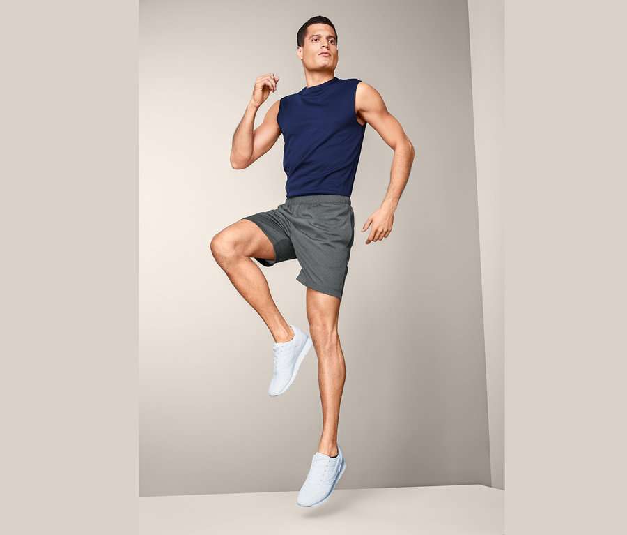 Mężczyzna w spodenkach sportowych i podkoszulku pozuje w studio.