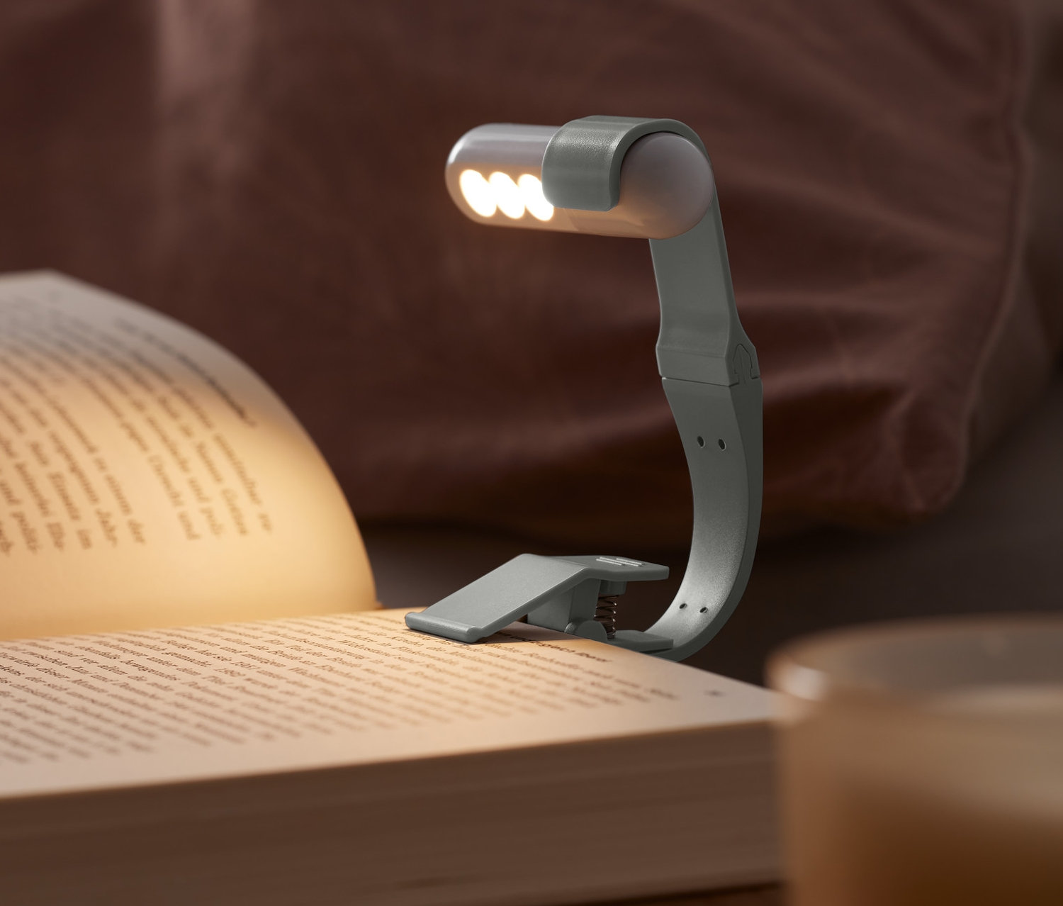 Lampka LED do czytania z akumulatorem przymocowana do książki leżącej na stoliku nocnym.