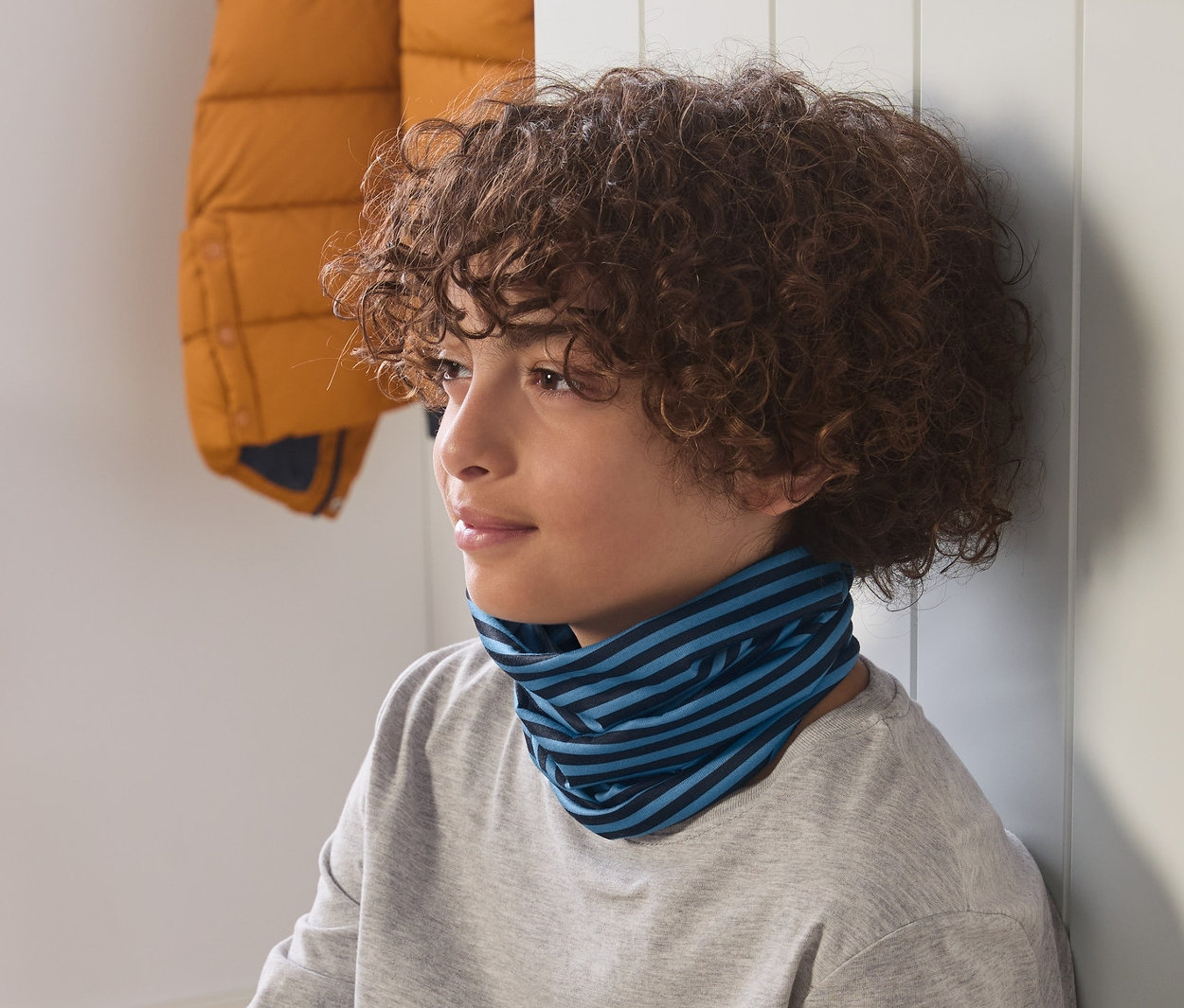Chłopiec siedzi, nosi chustę wielofunkcyjną w paski na szyi.