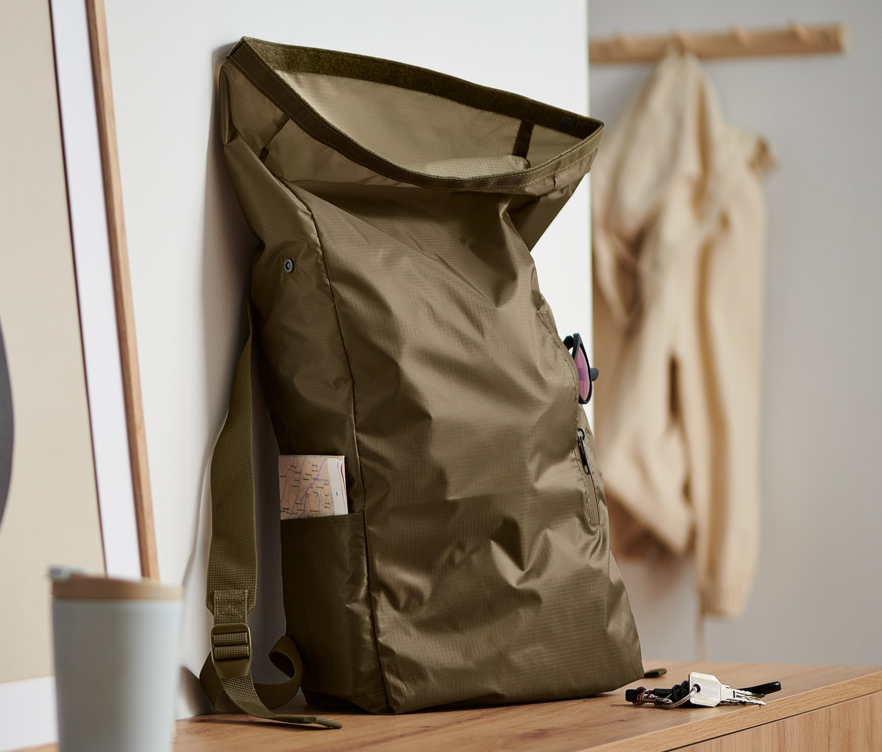 Khaki zwijany plecak oparty o ścianę obok abstrakcyjnej grafiki.