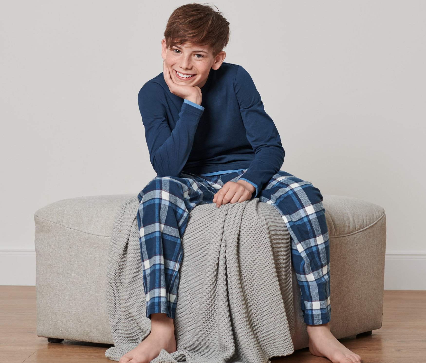 Chłopiec siedzi na beżowym pufie i ma na sobie dziecięcą piżamę flanelową.