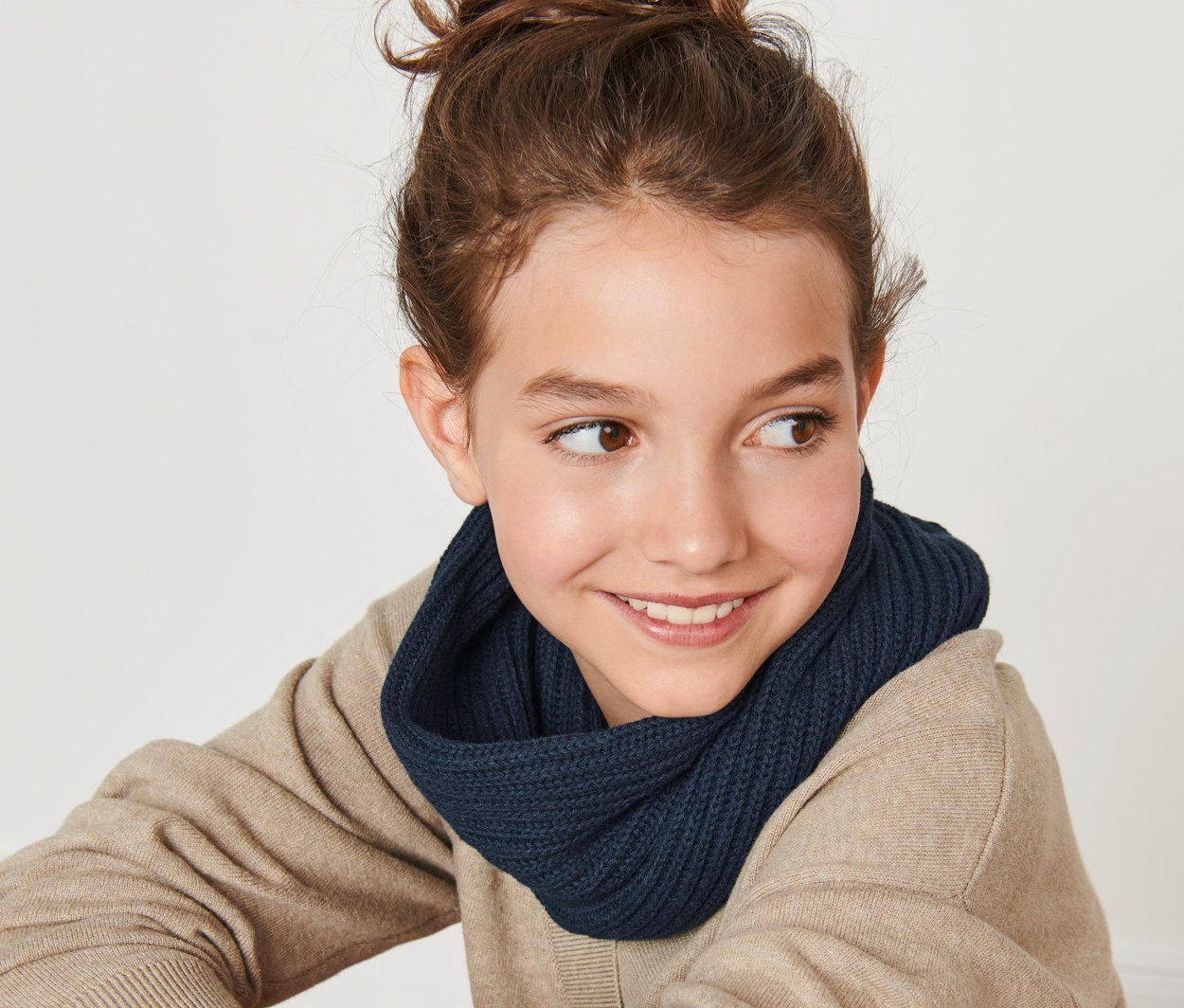 Uśmiechnięta nastolatka siedzi tyłem do kamery i ma na sobie szal-komin z dzianiny.