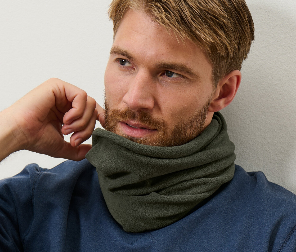 Mężczyzna z brązowymi włosami i brodą ma na sobie niebieską bluzę i termoaktywny komin z polaru.