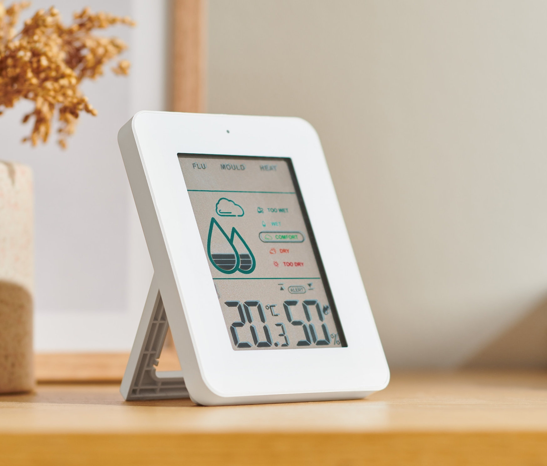 Higrometr cyfrowy z czujnikiem pleśni stoi na drewnianym stole obok wazonu z kwiatami.