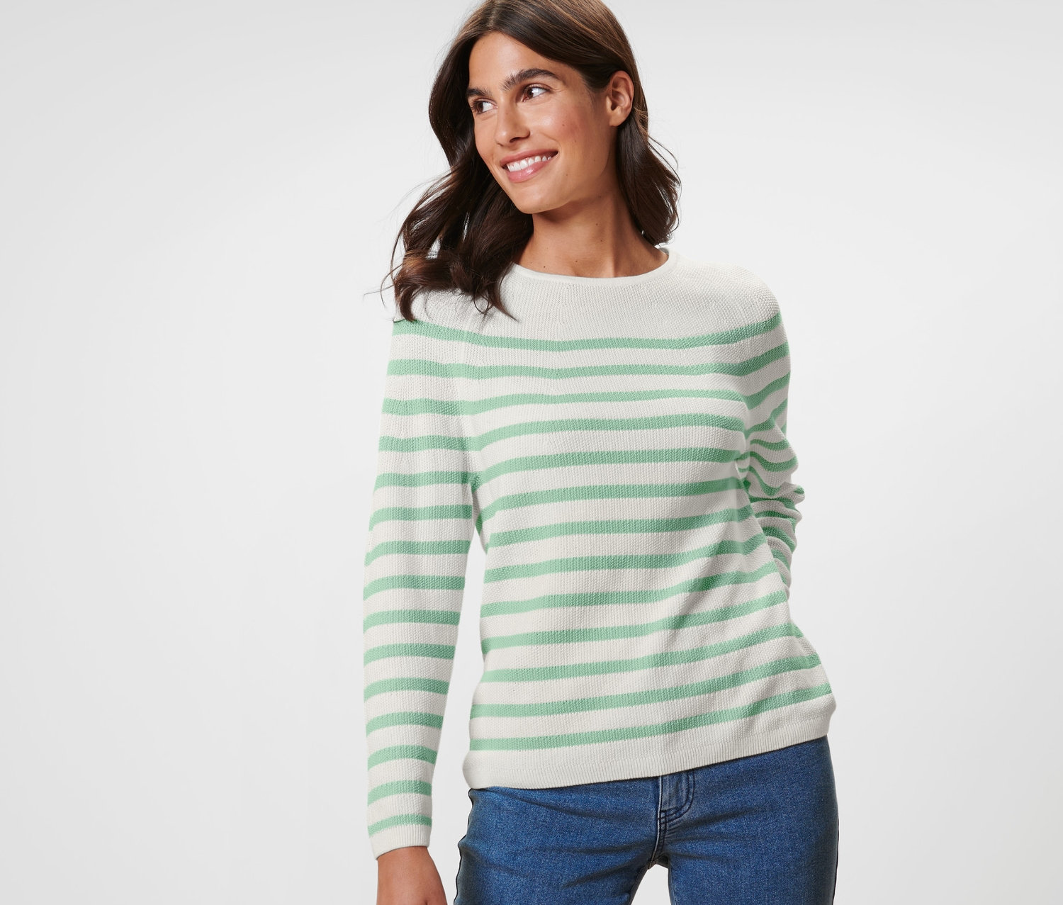 Uśmiechnięta kobieta pozuje w swetrze z dzianiny w paski i niebieskich dżinsach.