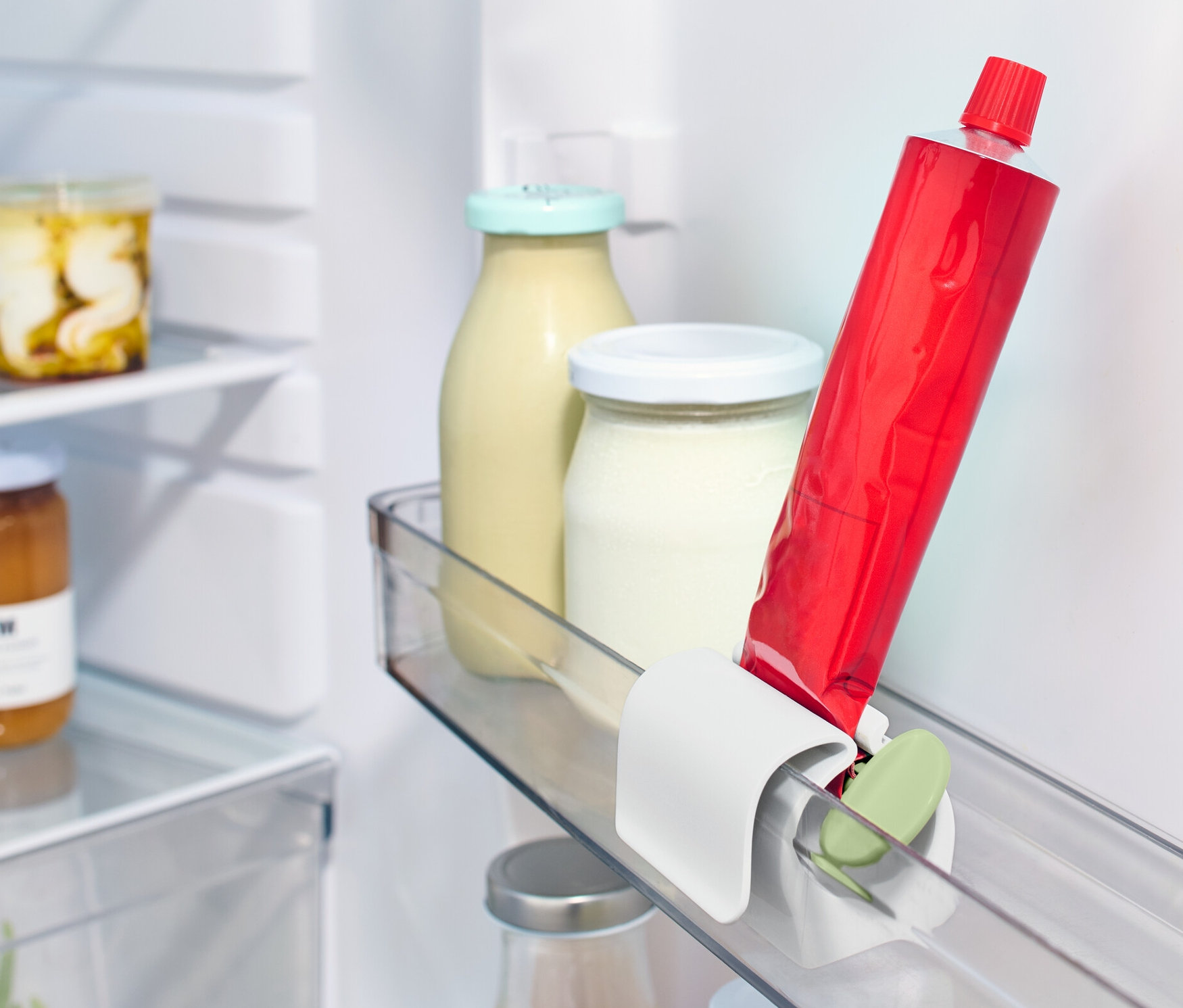Czerwona tuba umieszczona w wyciskaczu do tubek z klipsem do lodówki na półce lodówki obok innych produktów spożywczych.