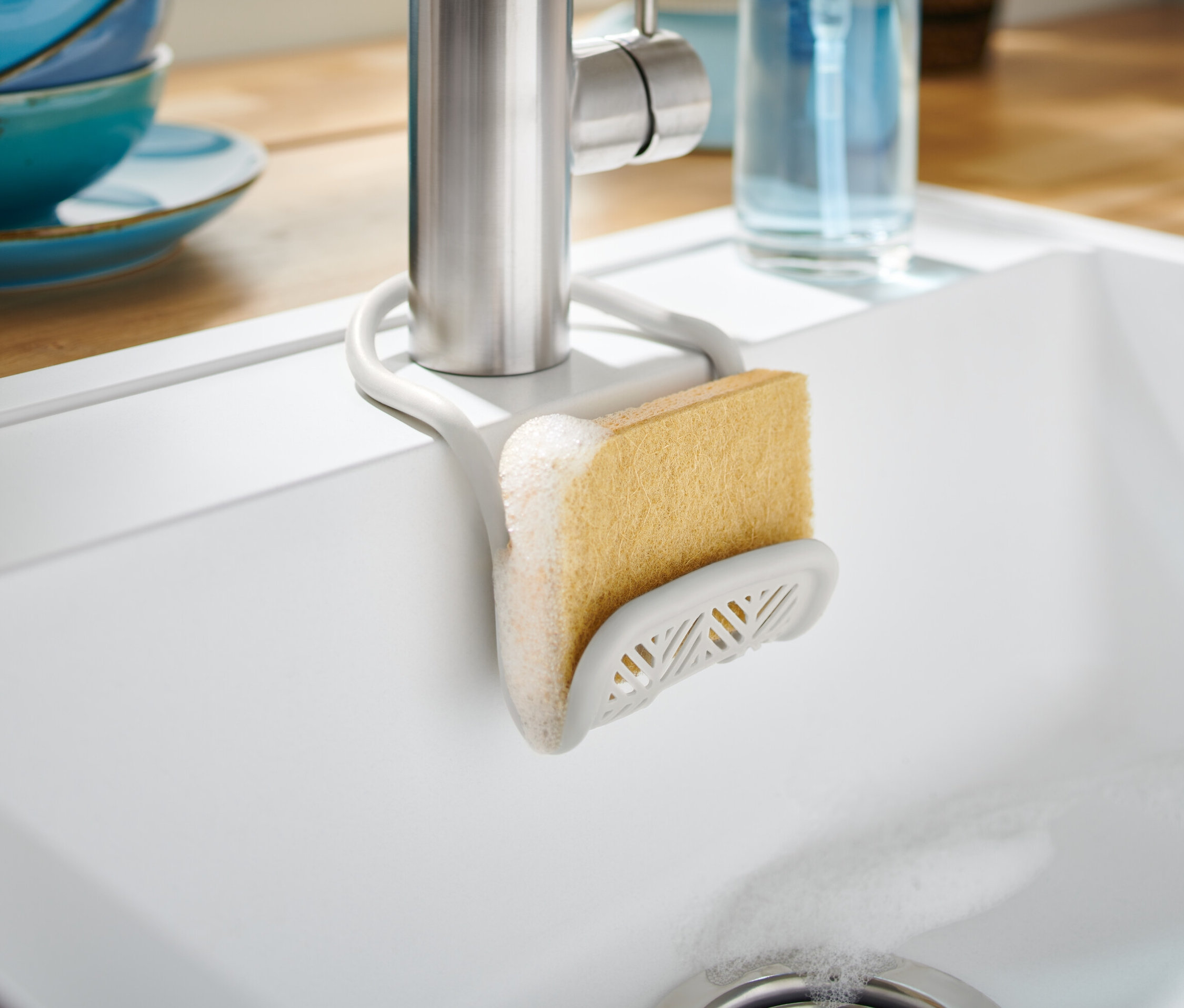 Organizer do zlewu z gąbką przymocowany do kranu w białym zlewie.