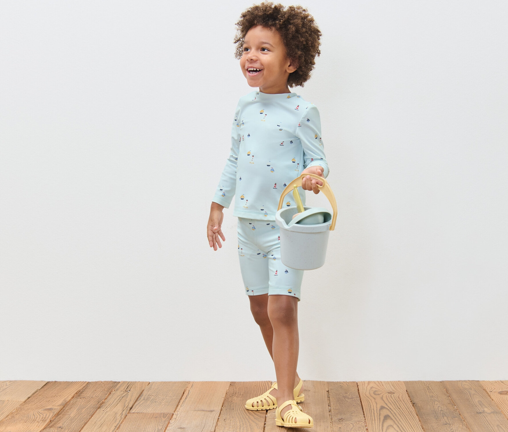 Chłopiec w komplecie dziecięcym z filtrem UV 80, wzór marynistyczny, trzyma wiaderko i łopatkę.