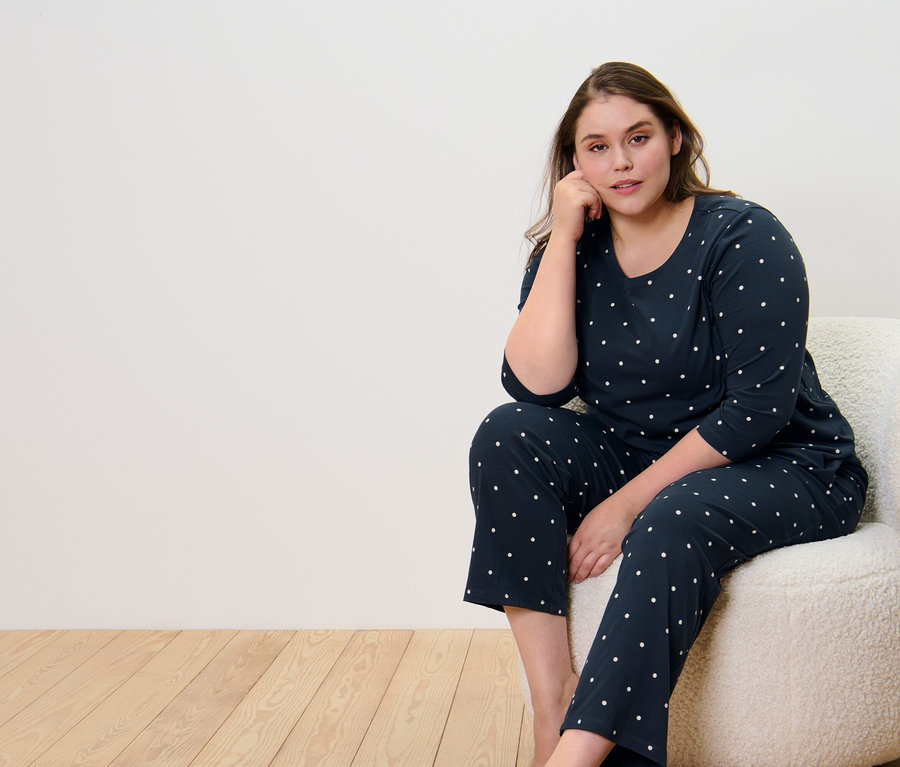 Kobieta siedzi na fotelu i ma na sobie piżamę w kropki.