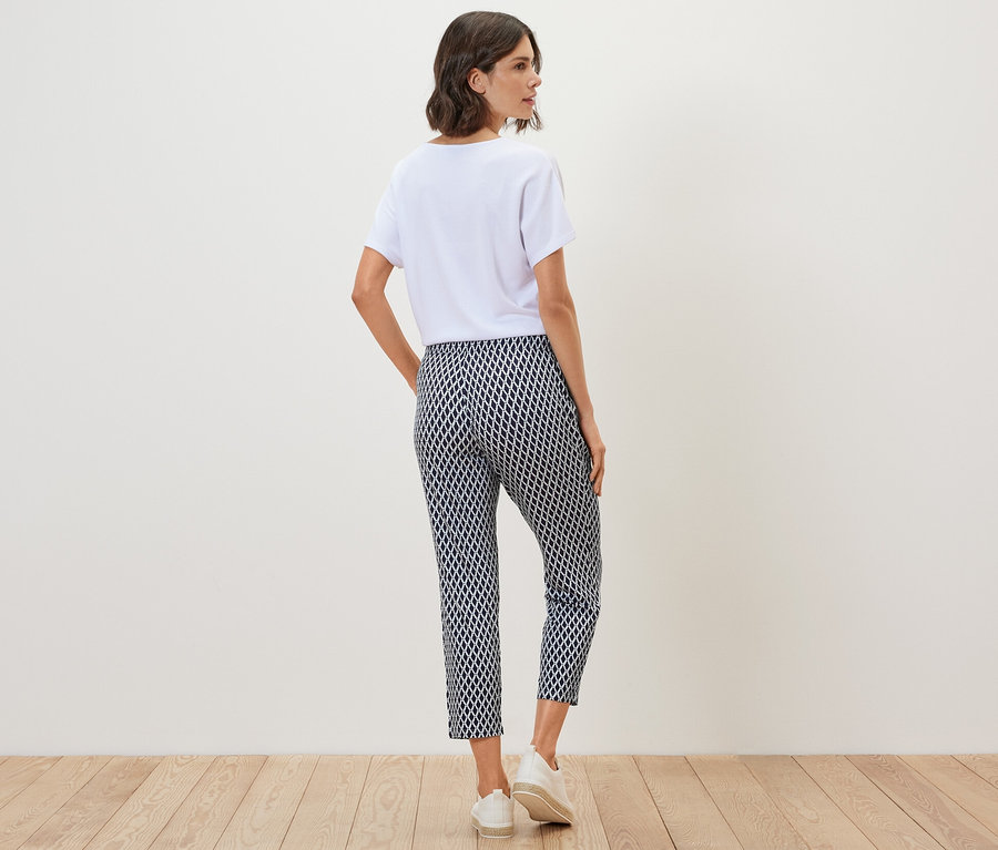 Kobieta stoi tyłem w białym t-shircie i wzorzystych spodniach z dżerseju.