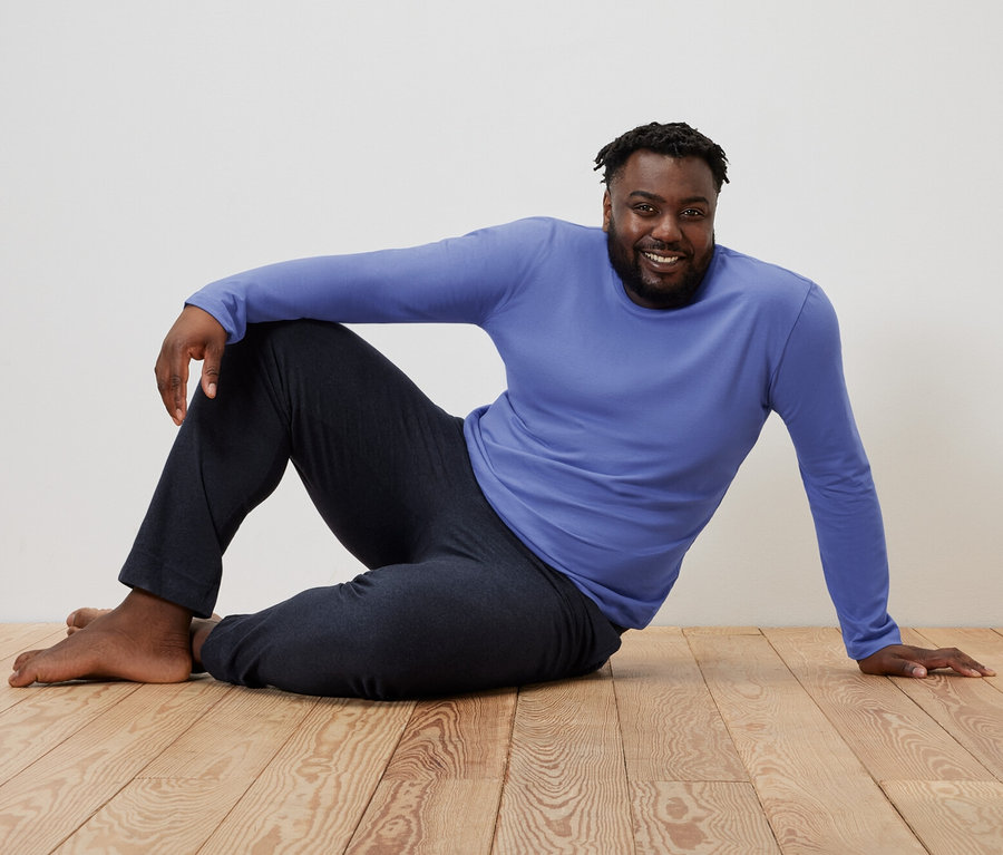 Mężczyzna siedzi na drewnianej podłodze w niebiesko-granatowej piżamie.