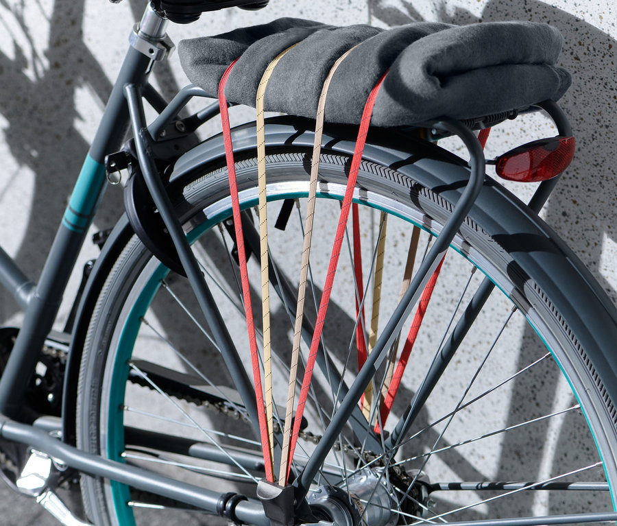 Szary koc przymocowany jest do bagażnika rowerowego za pomocą paska mocującego do roweru.