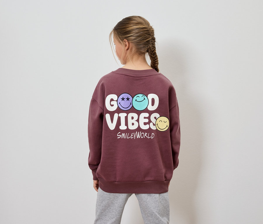 Dziewczynka tyłem do kamery ma na sobie bordową bluzę z napisem Good Vibes Smileyworld.