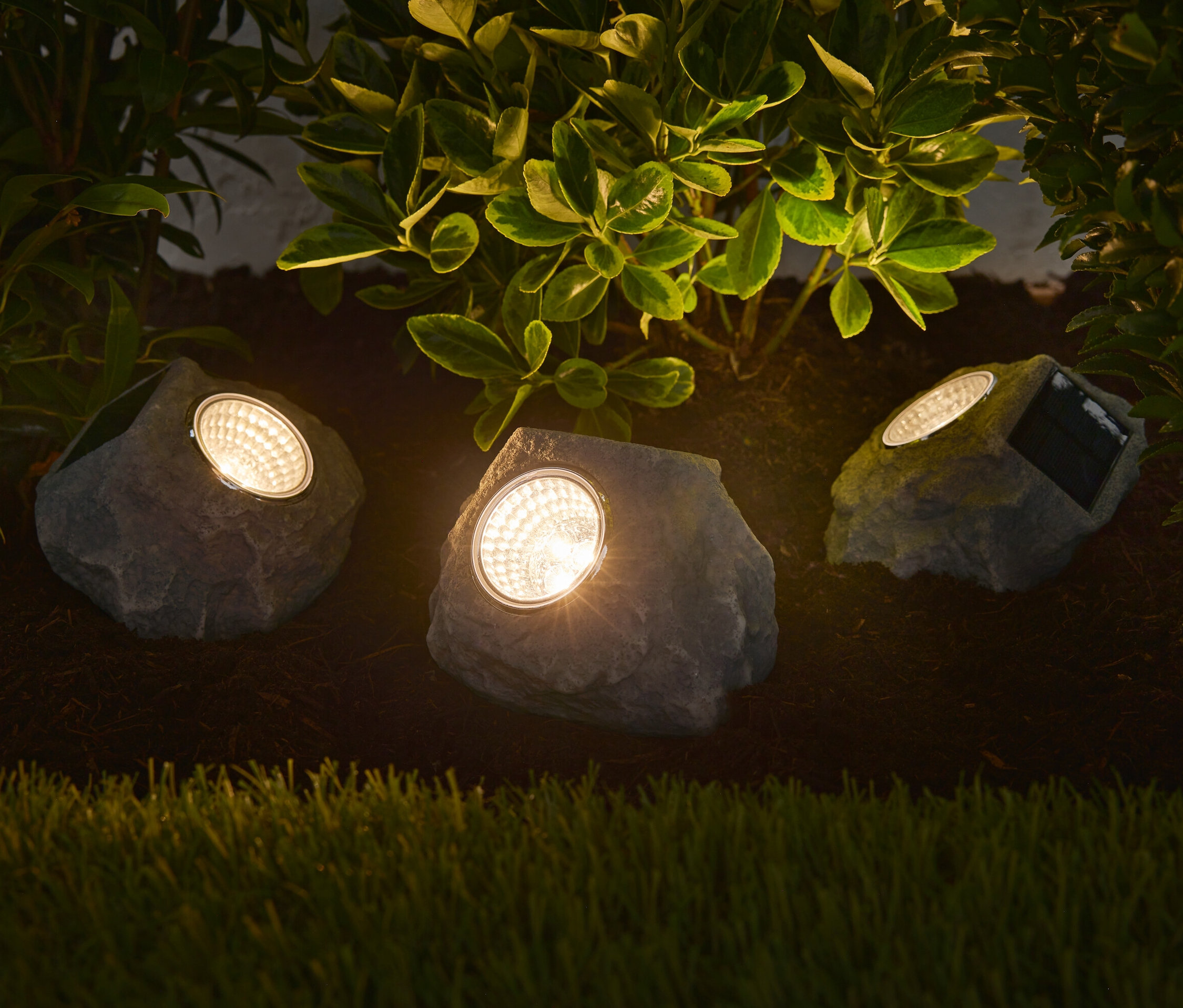 Trzy solarne kamienie LED premium oświetlają rabatę kwiatową.