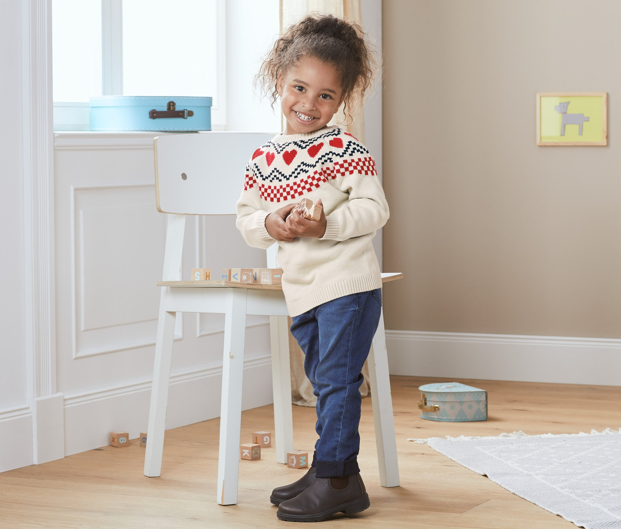 Dziewczynka stoi w swetrze z dzianiny z norweskim wzorem i bawi się drewnianymi klockami.