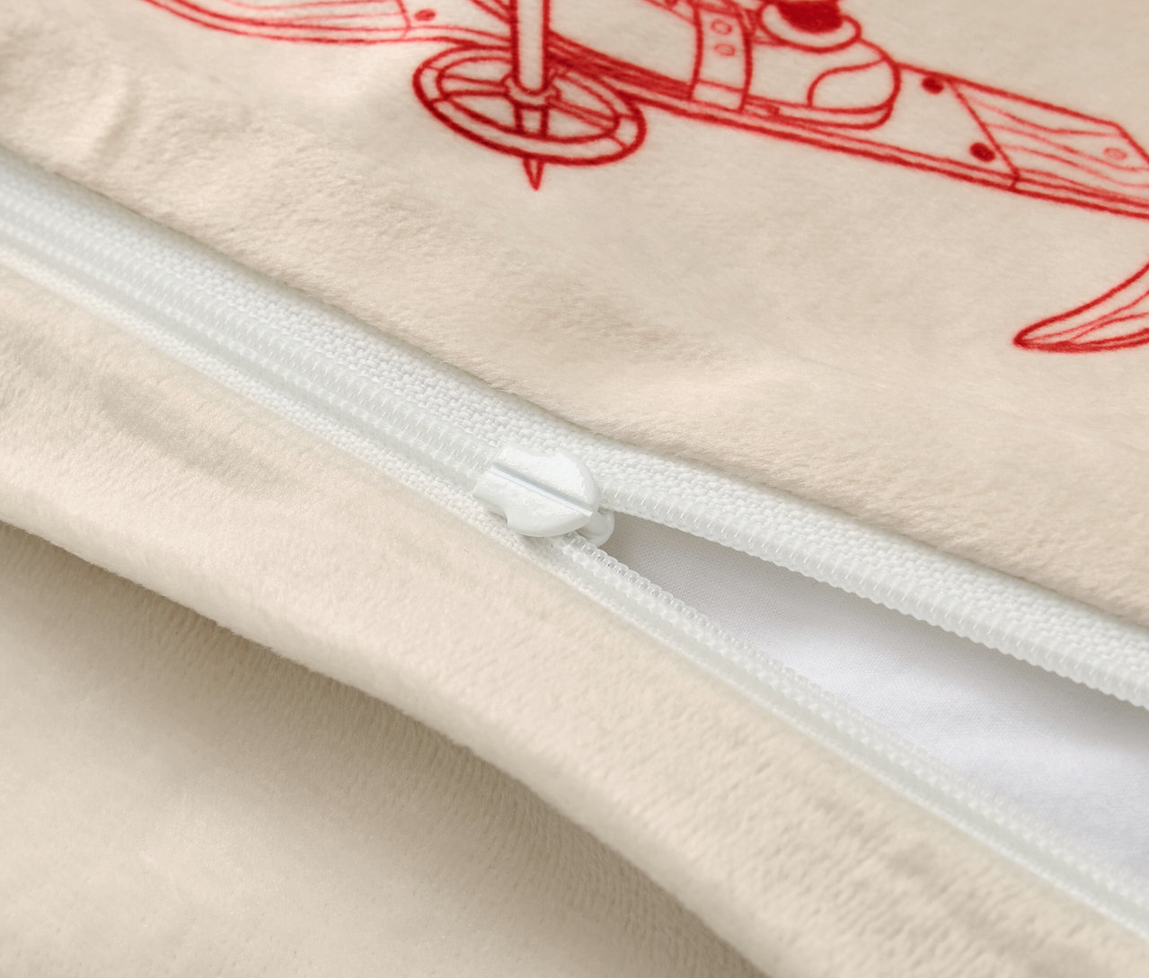 Beżowa poszewka na poduszkę z czerwoną ilustracją narciarza i białym zamkiem błyskawicznym.