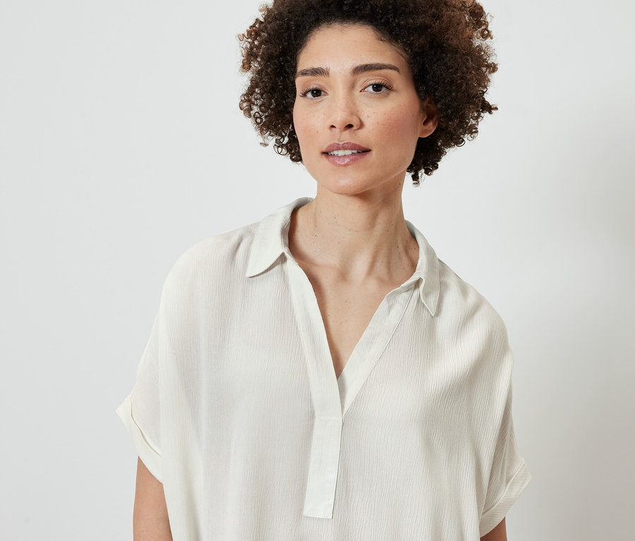 Portret kobiety o brązowych kręconych włosach w kremowej bluzce.