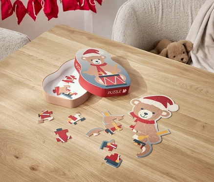 Na stole leżą rozłożone puzzle z motywem misia w czapce Świętego Mikołaja oraz jego pudełko.