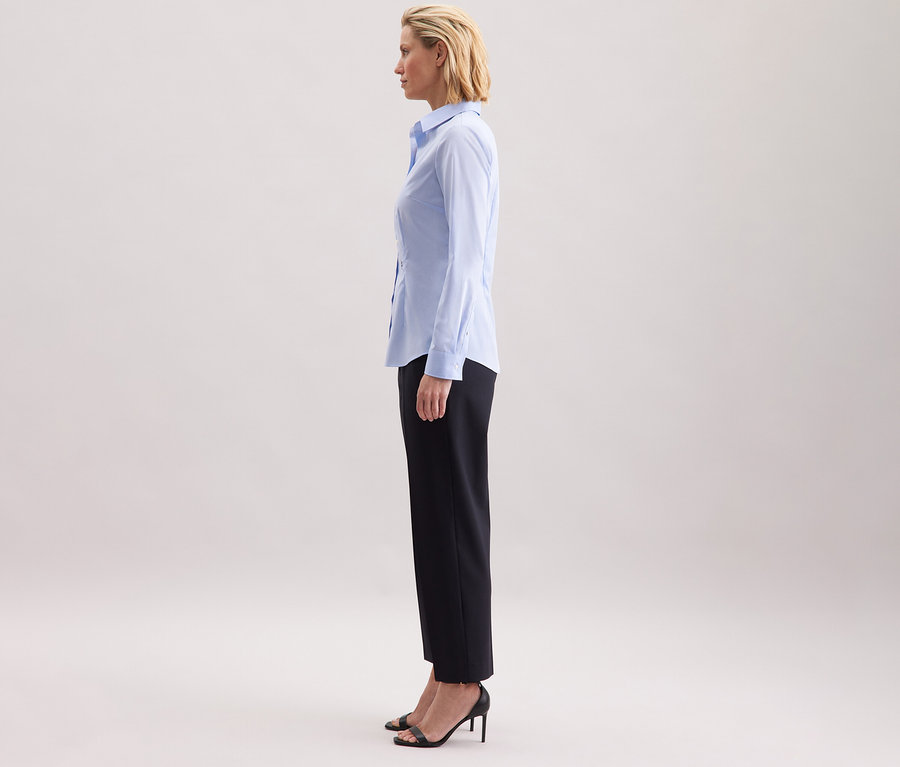 Kobieta stoi bokiem i ma na sobie jasnoniebieską bluzkę Seidensticker Slim Fit non iron.