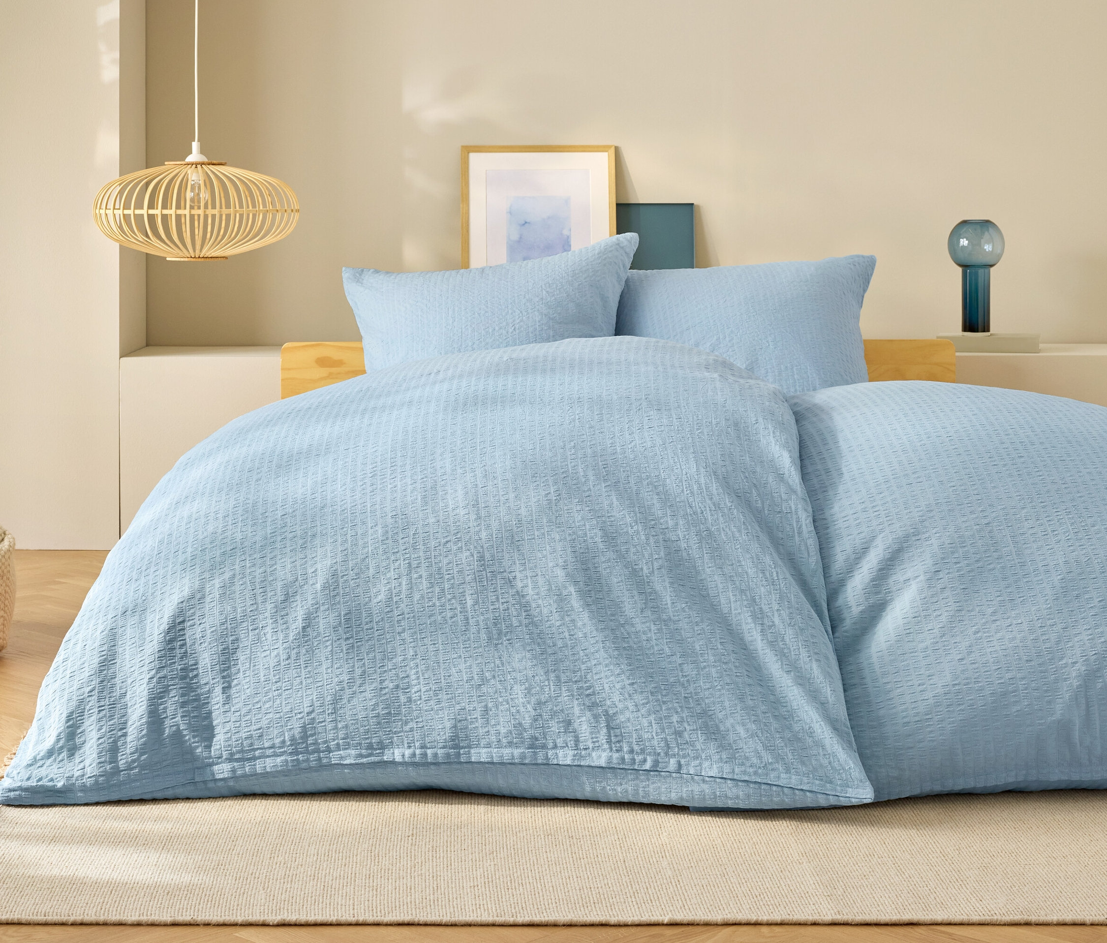 Jasnoniebieska pościel na łóżku z poduszkami i lampą w tle.