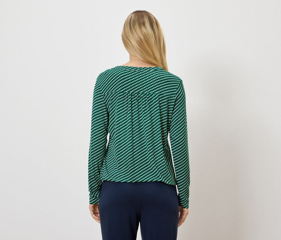 Kobieta ma na sobie zieloną bluzkę w paski z długim rękawem i granatowe spodnie.