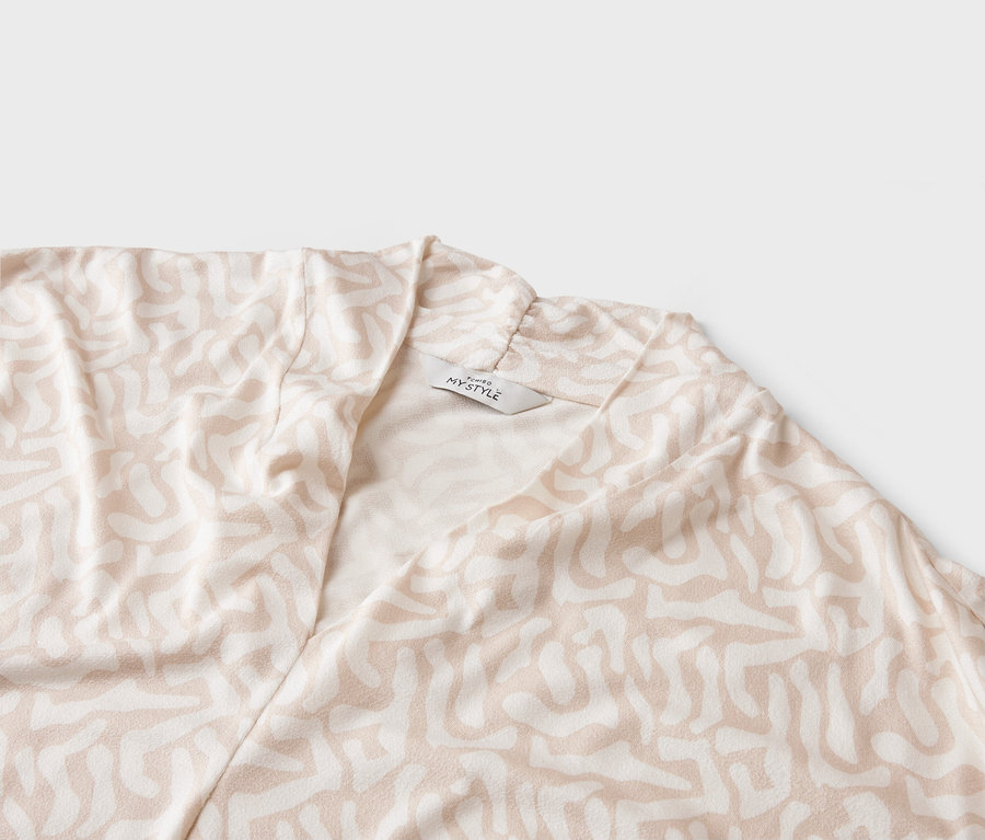 Zbliżenie jasnego płaszcza ze abstrakcyjnym wzorem i metką 'MY STYLE'.