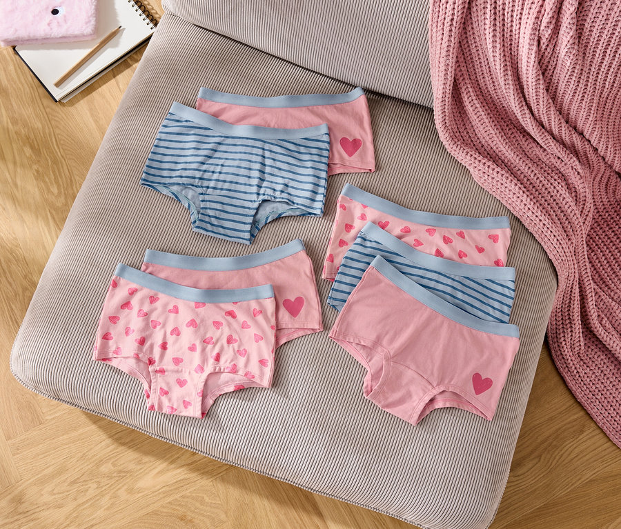 Na pufie w paski leży sześć par dziewczęcych majtek w kolorze różowym i niebieskim.