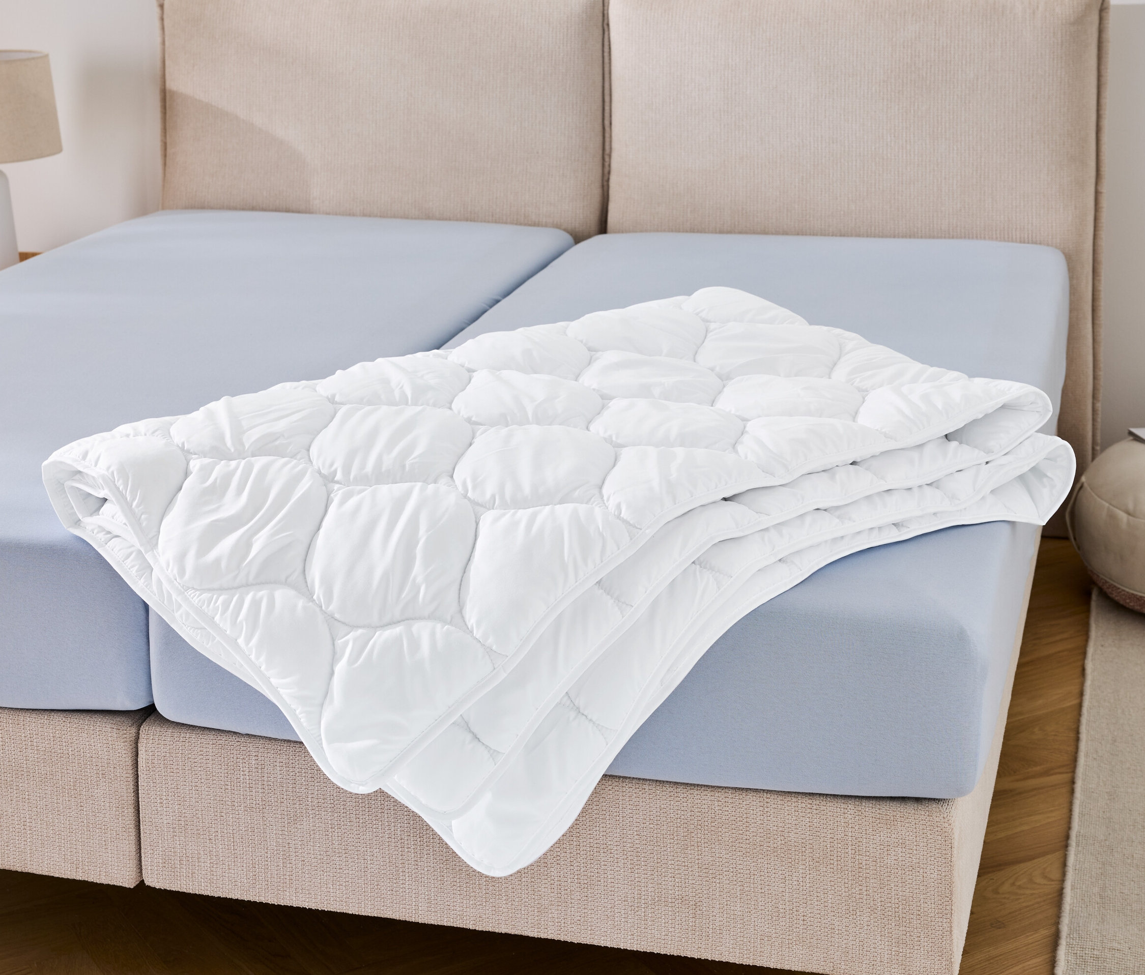 Na niebieskim prześcieradle leży złożona kołdra odporna na pranie w wysokiej temperaturze w rozmiarze niestandardowym.