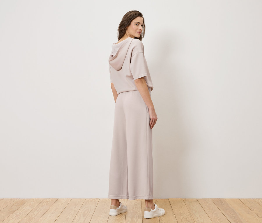 Kobieta stoi w jasno-różowym garniturze i białych tenisówkach, odwracając głowę przez ramię.