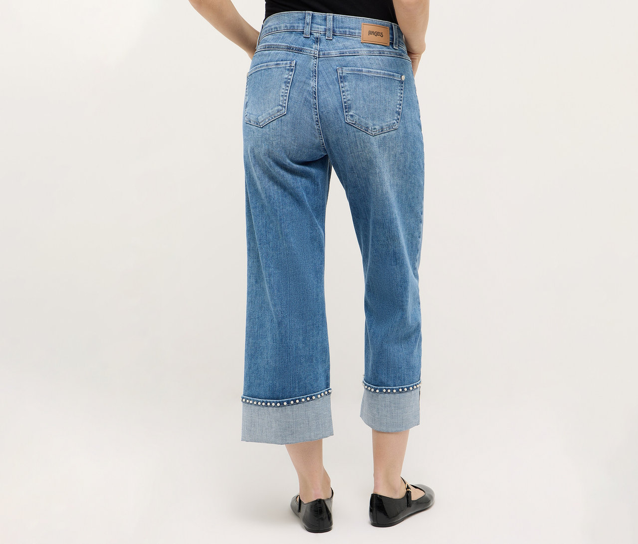 Osoba widziana od tyłu, ubrana w dżinsy Angels „Linn Cool” i czarne buty na neutralnym tle.