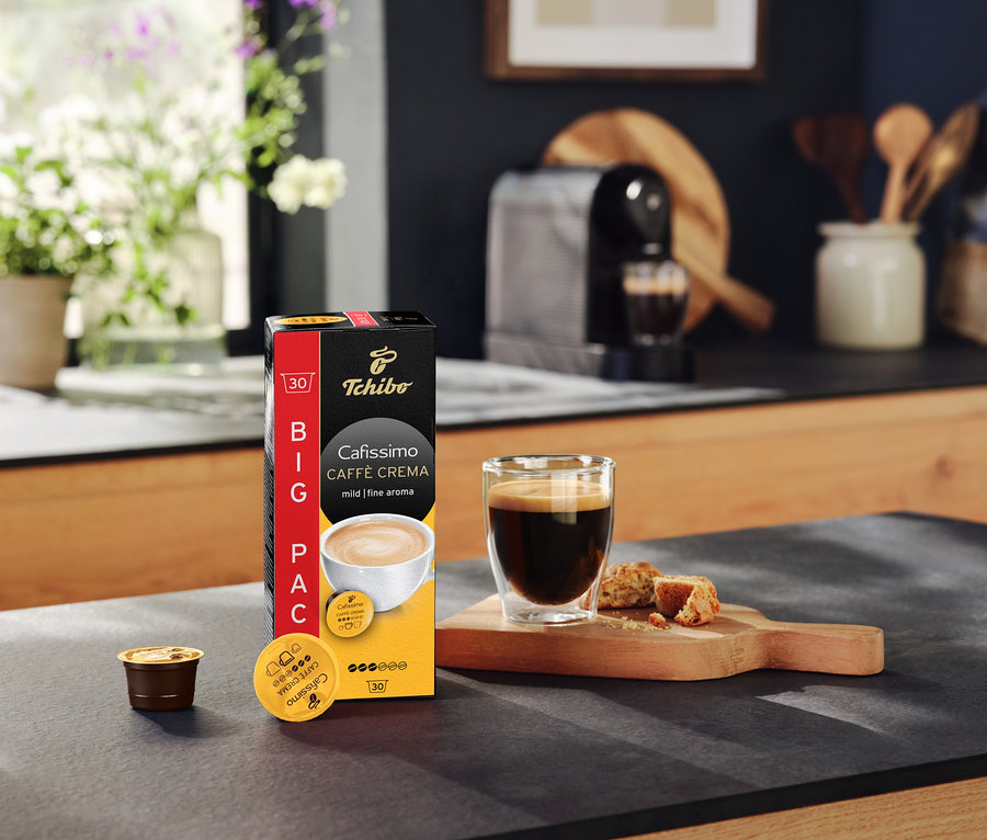 Opakowanie kapsułek Cafissimo Caffè Crema mild, filiżanka kawy i ekspres do kawy na blacie kuchennym.