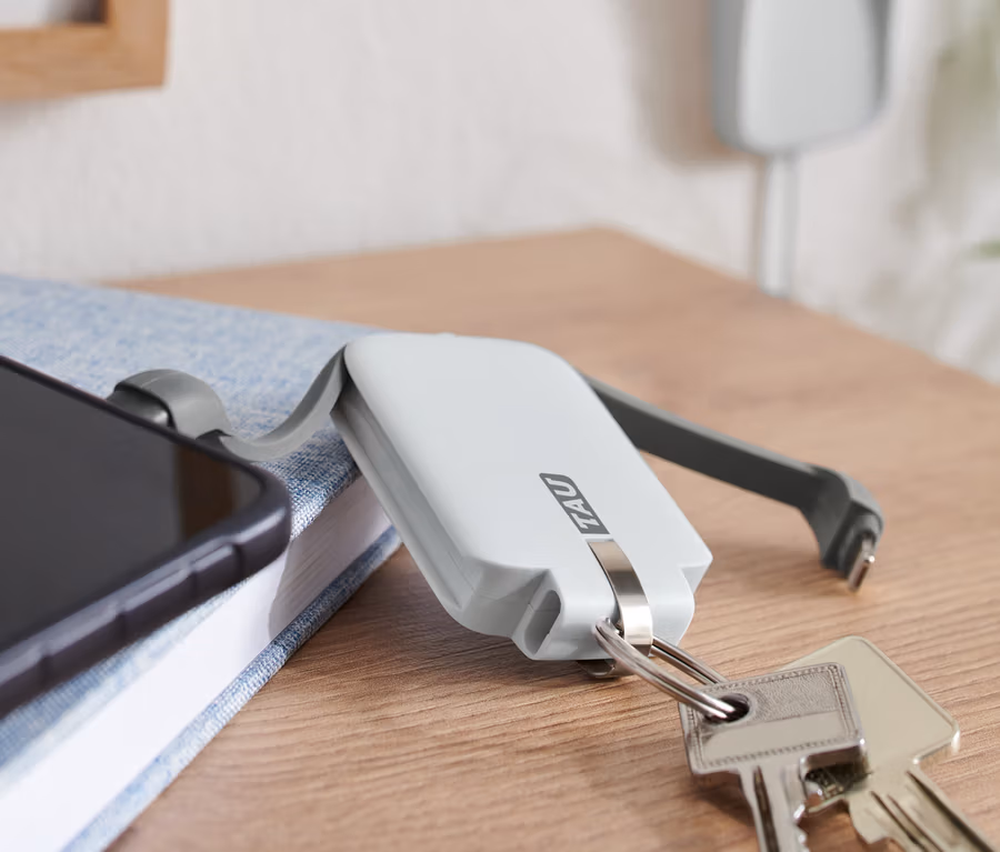 Telefon leży na niebieskiej książce obok kluczy i białego powerbanku TAU® 3-in-1-Keychain.