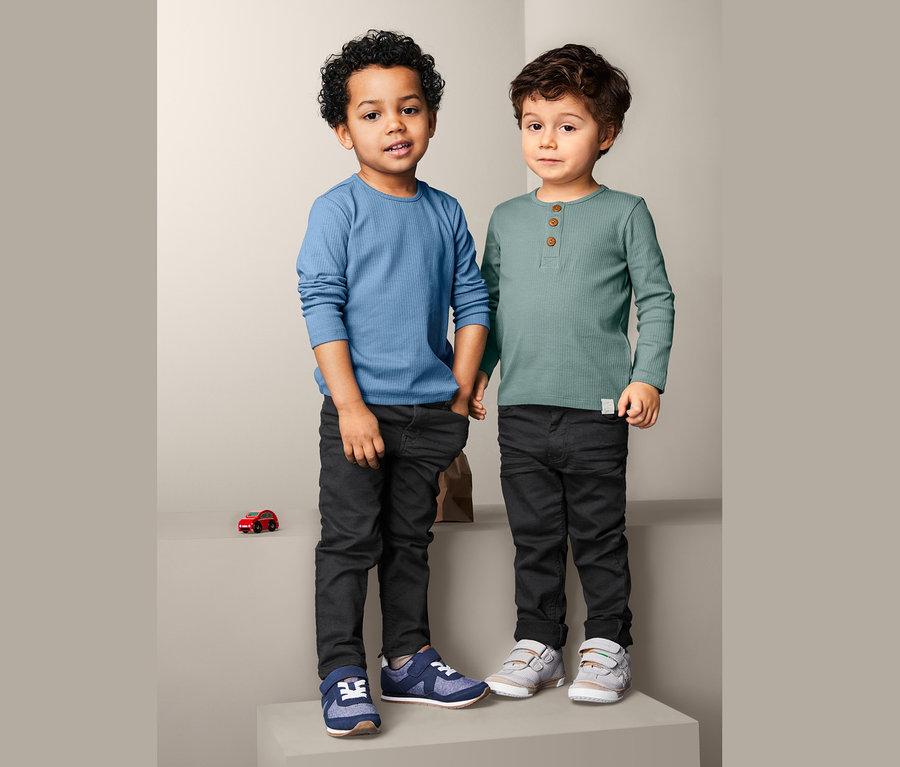 Dwóch chłopców stoi obok siebie, ubrani w dziecięce koszulki z długimi rękawami, 2 sztuki i czarne spodnie.