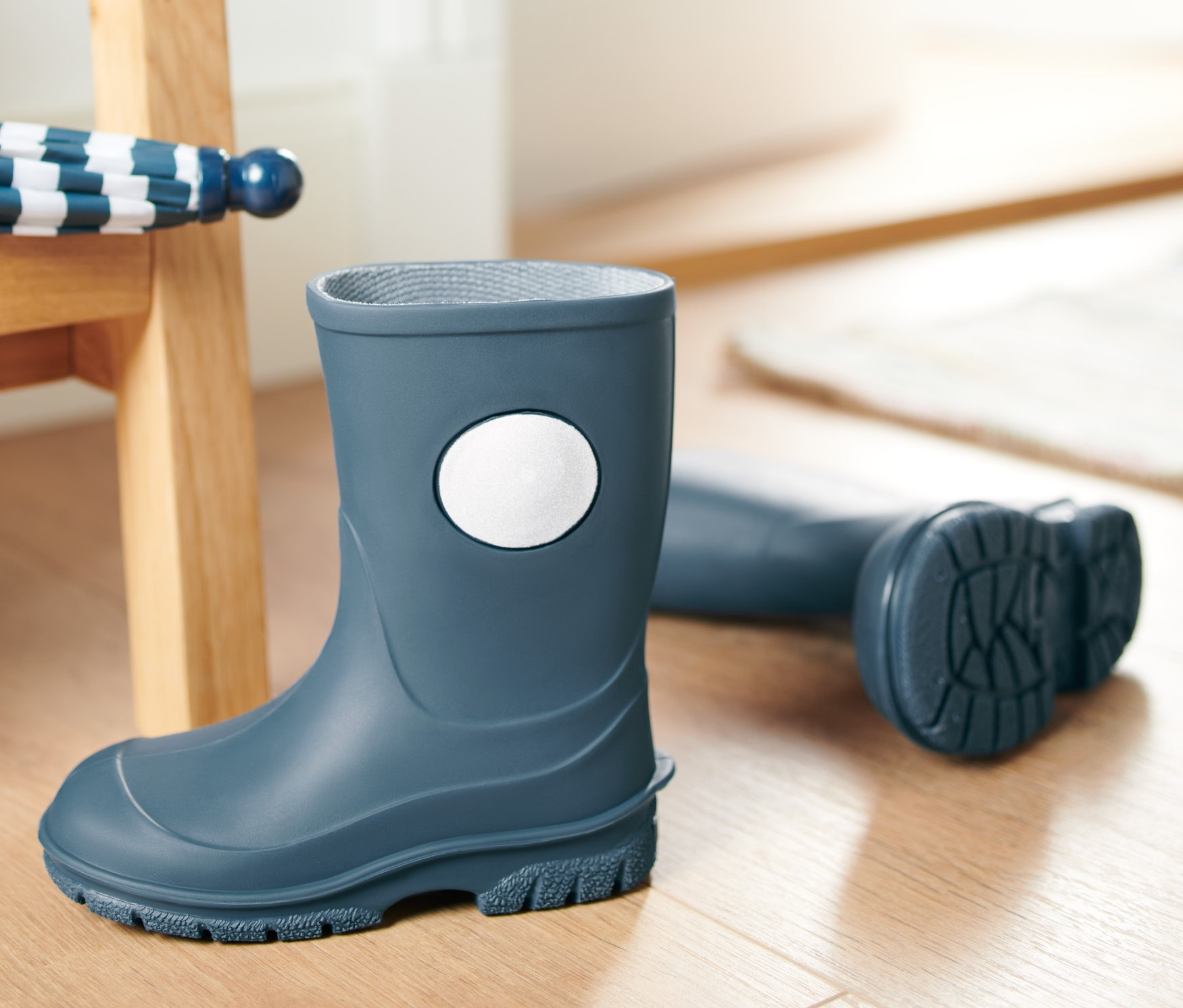 Niebieski kalosz stoi na podłodze, obok leży parasol i zielone wiadro.