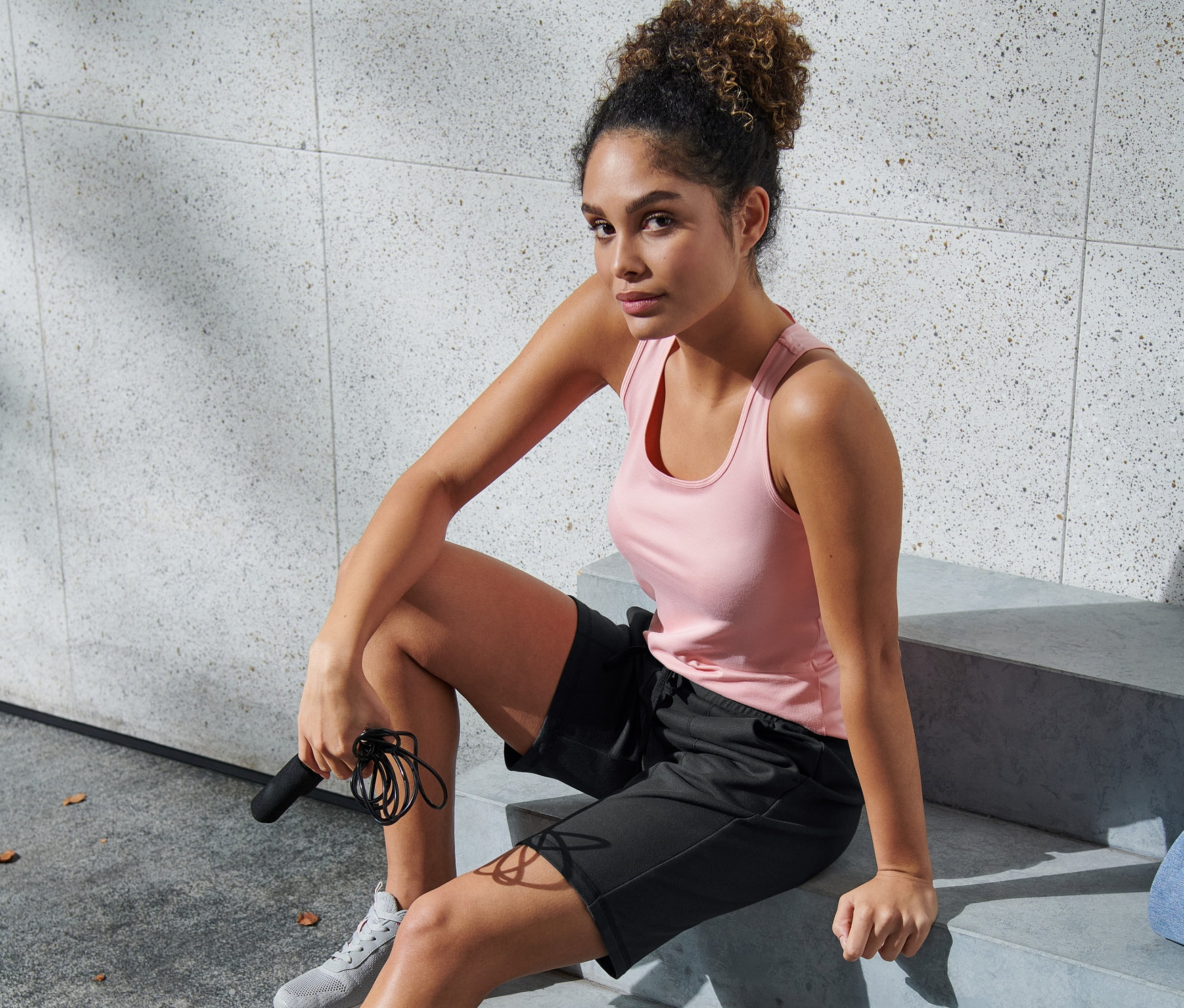 Kobieta siedzi na schodach w brązowo-czarnych szortach funkcyjnych, trzymając skakankę.