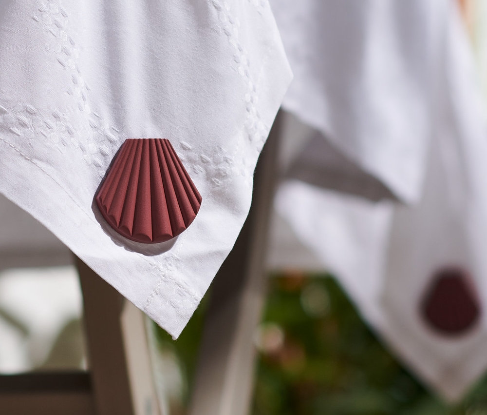 Krawędź stołu z białym obrusem obciążonym brązowymi obciążnikami do obrusu w kształcie muszli, 4 sztuki.