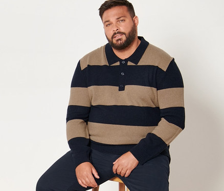 Mężczyzna siedzi na stołku, ubrany w granatowe spodnie chino i sweter z zawartością kaszmiru w paski.