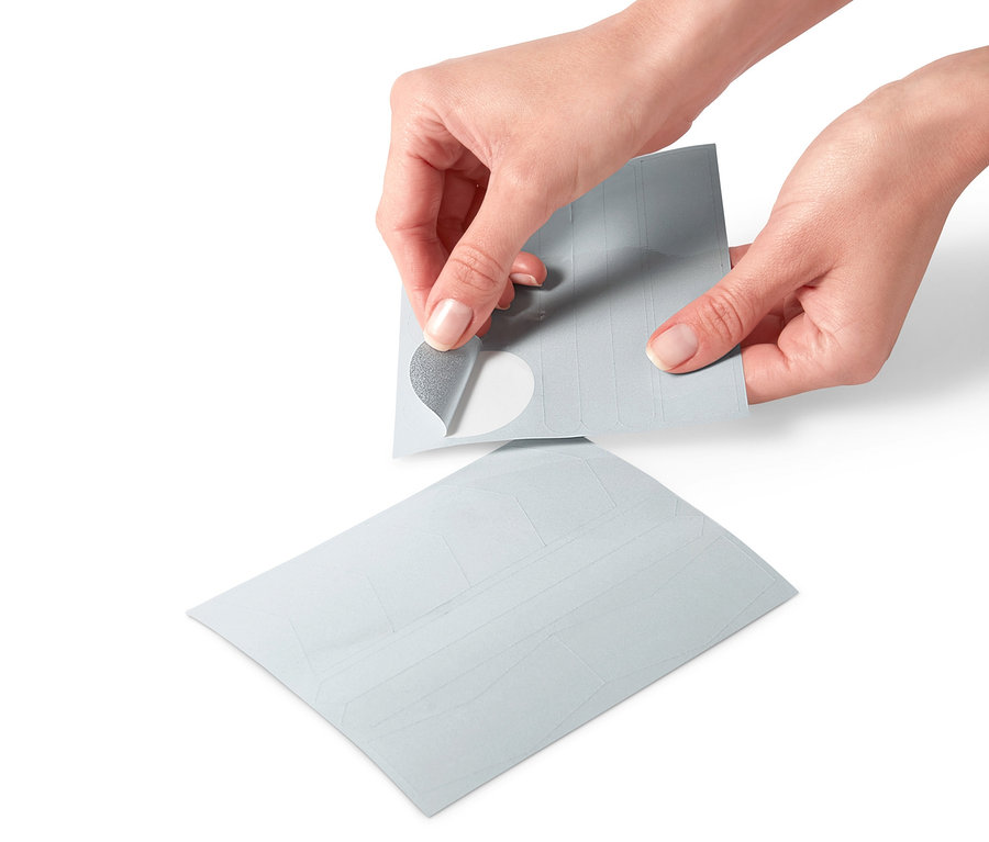 Dłonie odklejają naklejkę odblaskową z arkusza naklejek odblaskowych, 16 sztuk.