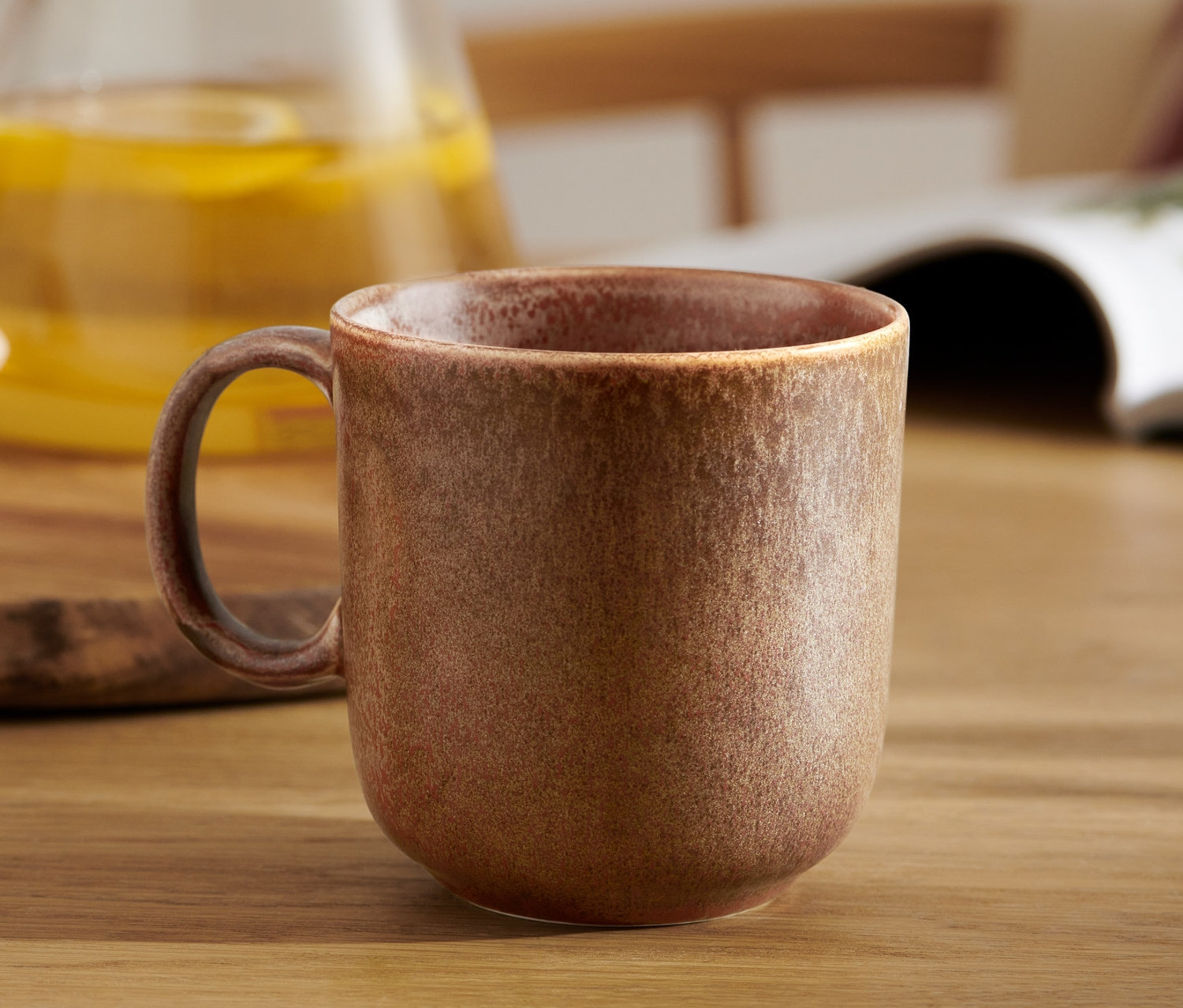 Brązowy kubek na stole z napojem i ciastkami w tle.